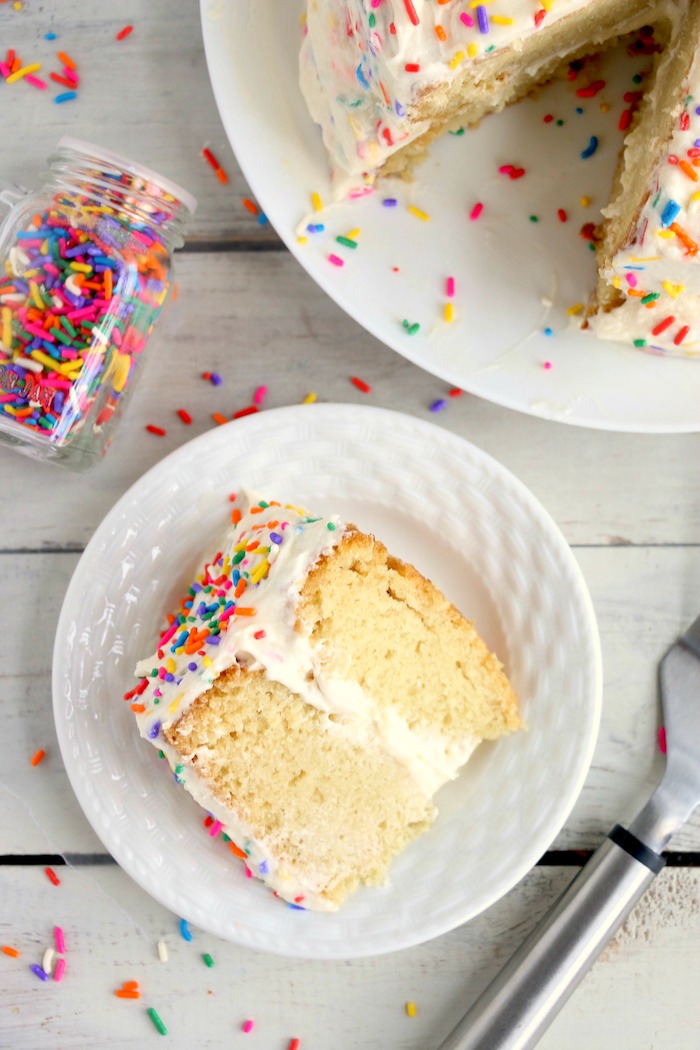 Piece of cake on plate next to bottle of sprinkles