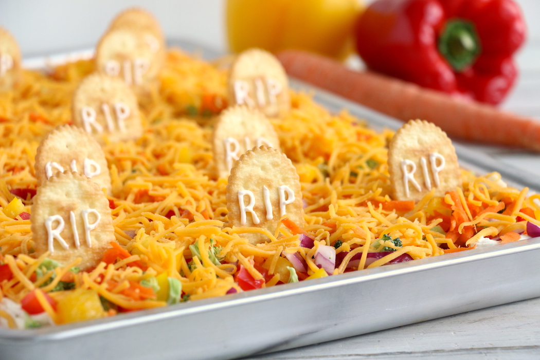 Halloween Veggie Pizza - A spooky themed graveyard pizza featuring a flavorful ranch cream cheese covered crust, topped with colorful veggies and "tombstone" crackers.