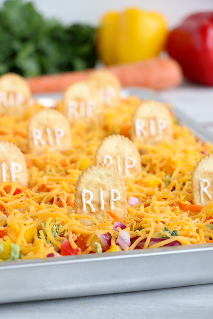 Halloween Veggie Pizza - A spooky themed graveyard pizza featuring a flavorful ranch cream cheese covered crust, topped with colorful veggies and "tombstone" crackers.