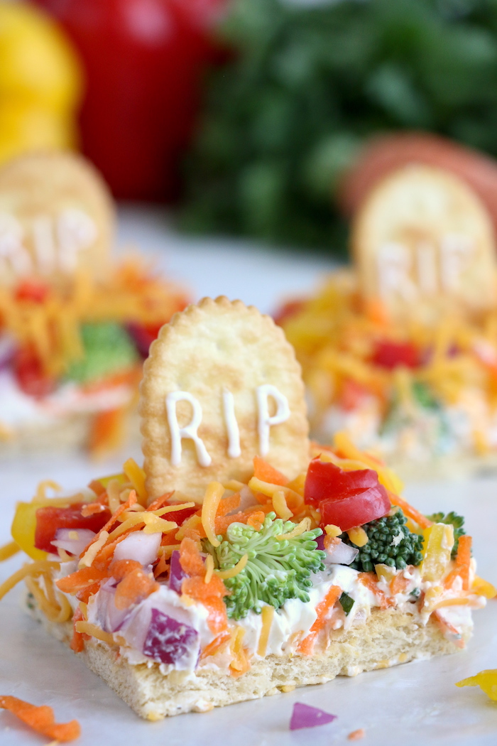 Halloween Veggie Pizza - A spooky themed graveyard pizza featuring a flavorful ranch cream cheese covered crust, topped with colorful veggies and "tombstone" crackers.